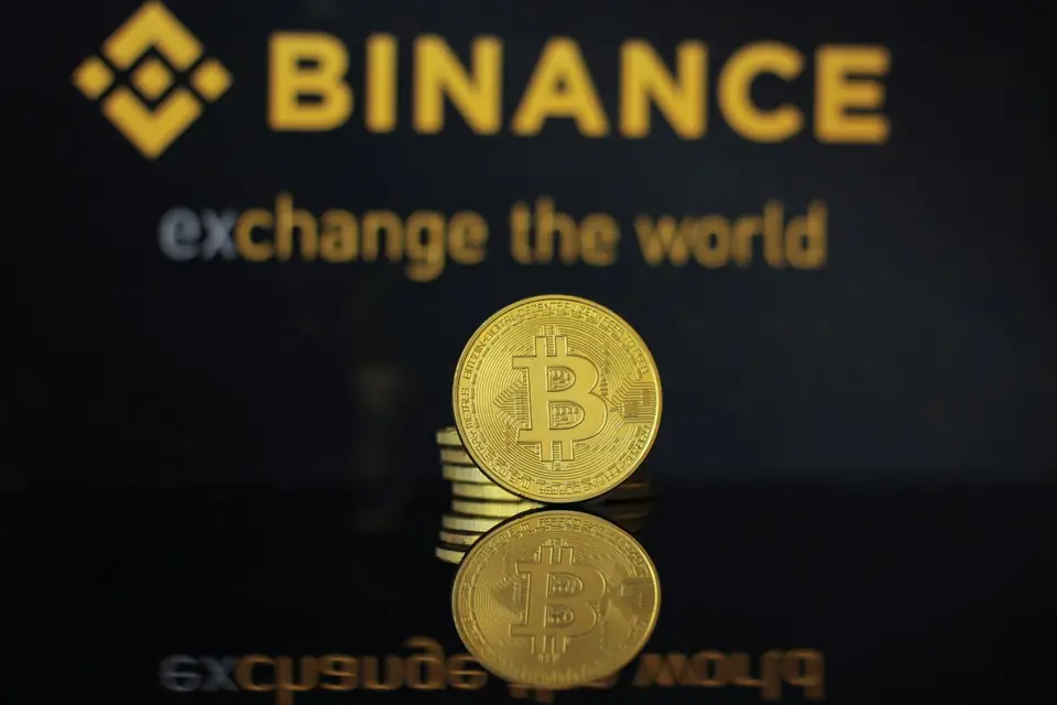 Moeda de bitcoin em frente ao logotipo da corretora Binance